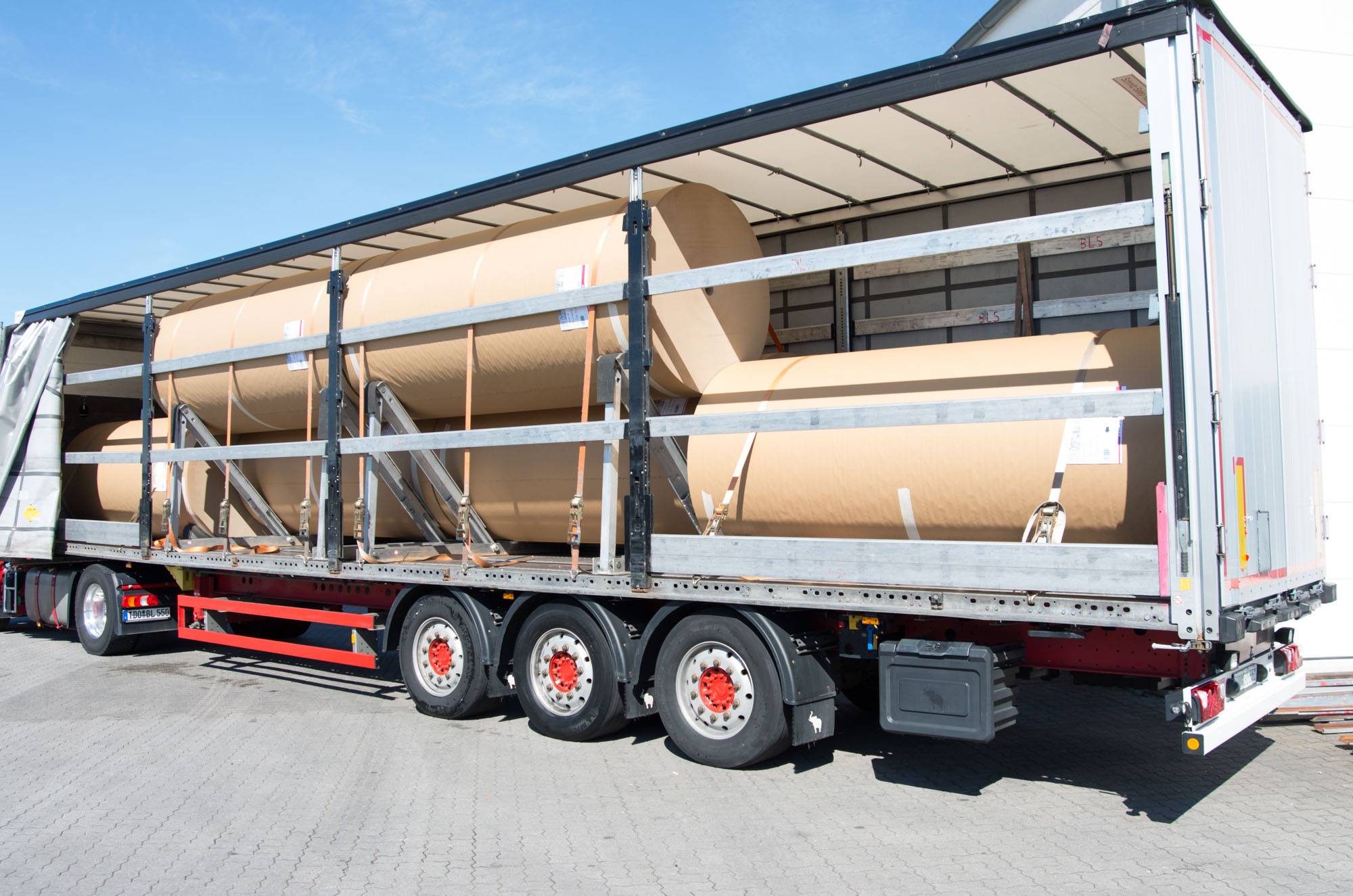Large kraft paper rolls loaded on tautliner truck for road transport